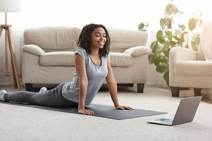 A smiling lady practicing Yoga with her laptop in front of her 